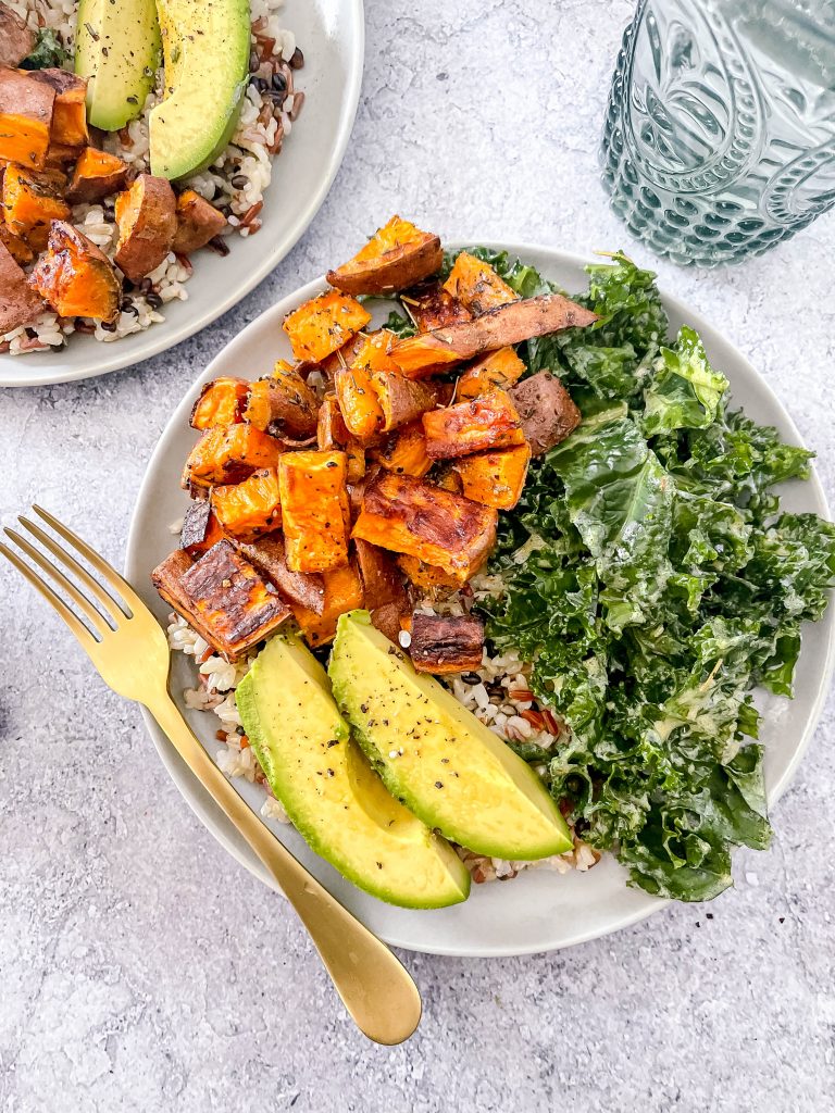 A bowl with brown rice, topped with roasted sweet potatoes, massaged kale, and vibrant avocado.
