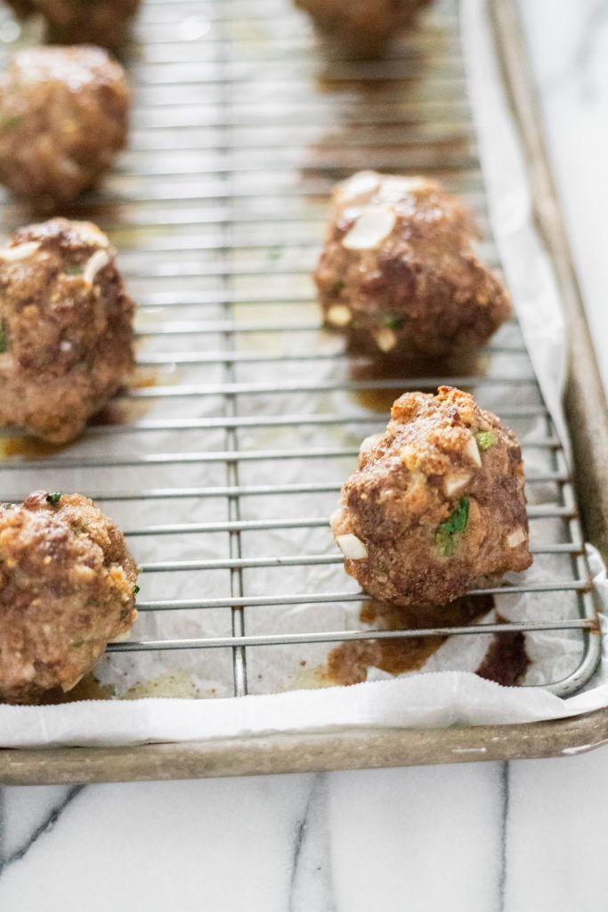 Cooked meatballs on a wire rack on a rimmed baking tray.
