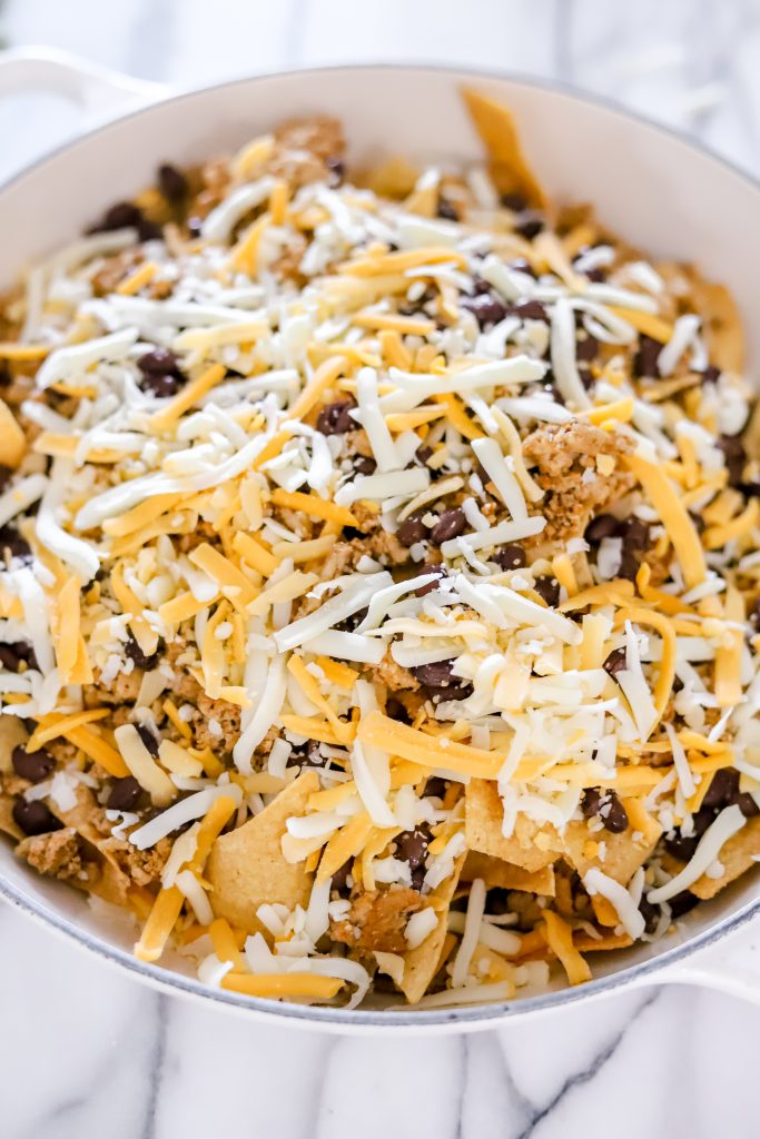 Tortilla chips on a white pan ontop of a marble backdrop with black beans and ground turkey ontop with unmelted cheese