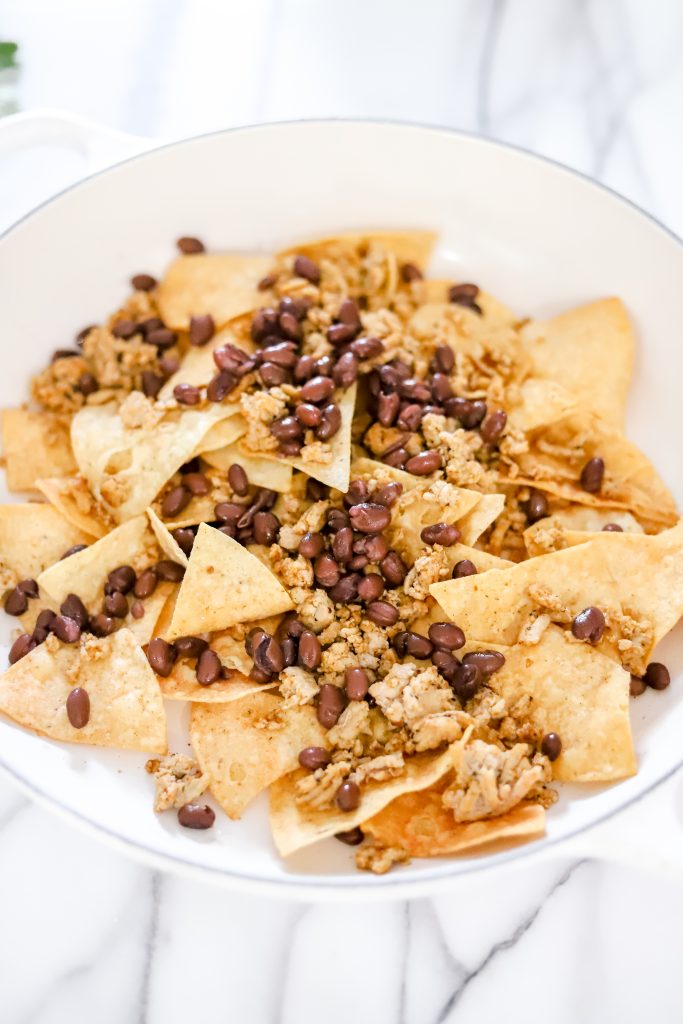 Tortilla chips on a white pan ontop of a marble backdrop with black beans and ground turkey ontop.