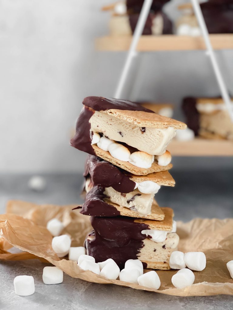 A stack of three ice cream sandwiches, made with graham crackers, and dipped in chocolate is in the front. 