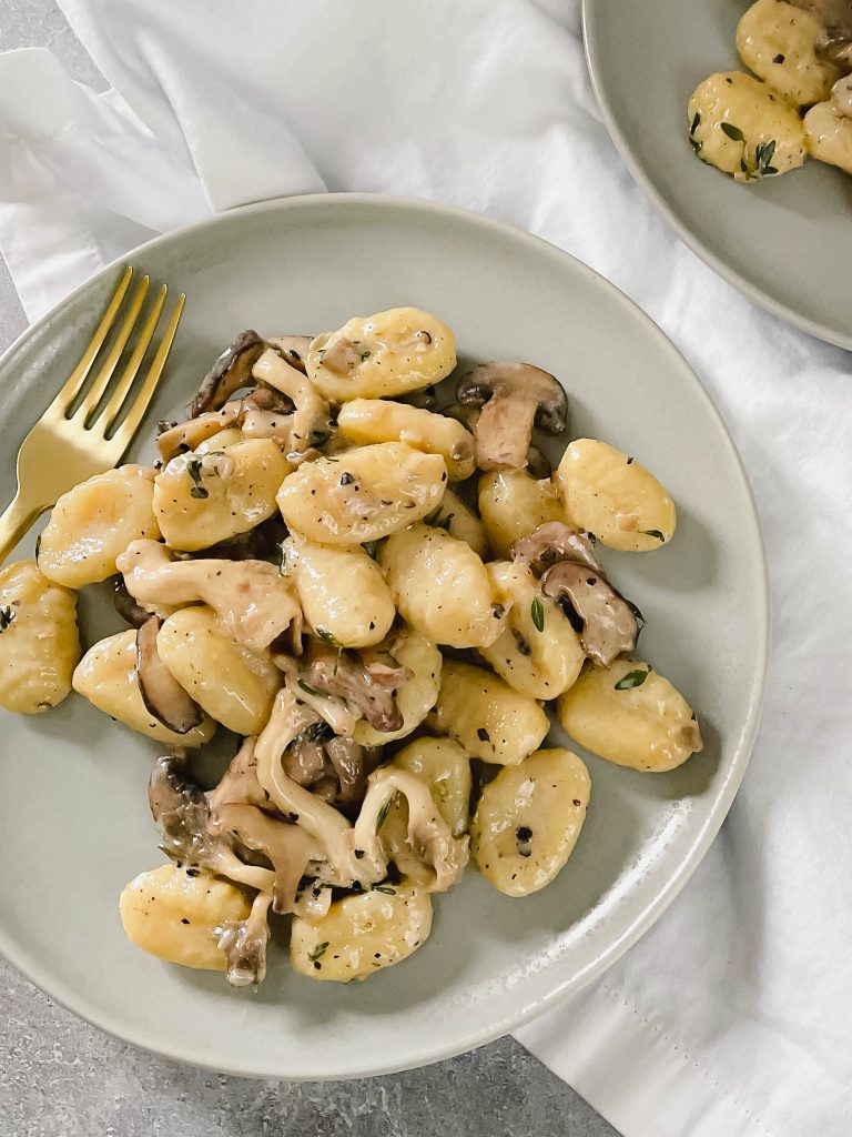 Two plates full of creamy gnocchi with mushrooms on a white background. 
