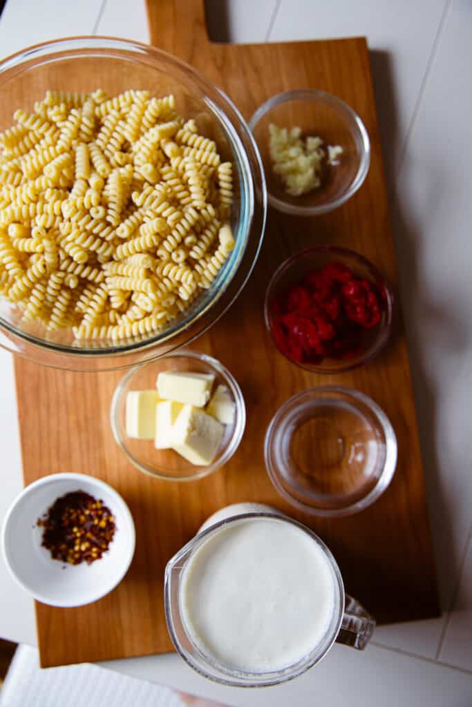 Ingredients for spicy tequila pasta in individual bowls on a cutting board: pasta, minced garlic, tomato paste, butter, red pepper flakes, tequila, heavy cream.