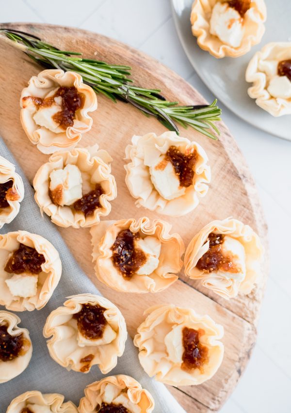 Mini tartlets on a wooden circular board with a sprig of rosemary.