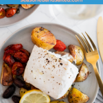 A gray plate with halibut, roasted potatoes, and vegetables. Gold flatware, and a glass of white wine.