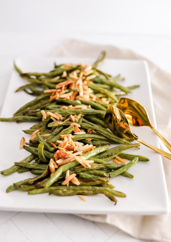 Roasted green beans topped with slivered almonds on a white rectangular plate.