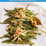 Roasted green beans topped with slivered almonds on a white rectangular plate.