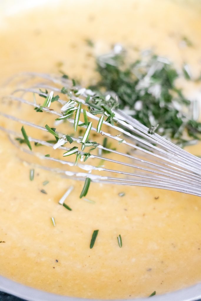 Butternut squash sauce simmering with a whisk with rosemary (how to make butternut squash macaroni and cheese process shot)