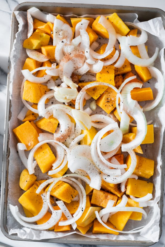 Raw chunks of butternut squash and onions on a baking sheet lined with parchment paper(how to make butternut squash macaroni and cheese process shot)