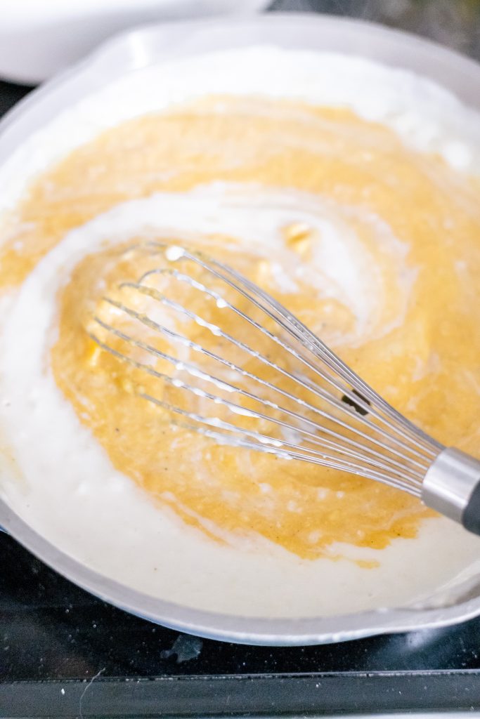 Whisk stirring milk into an orange butternut squash sauce over the stove (how to make butternut squash macaroni and cheese process shot)