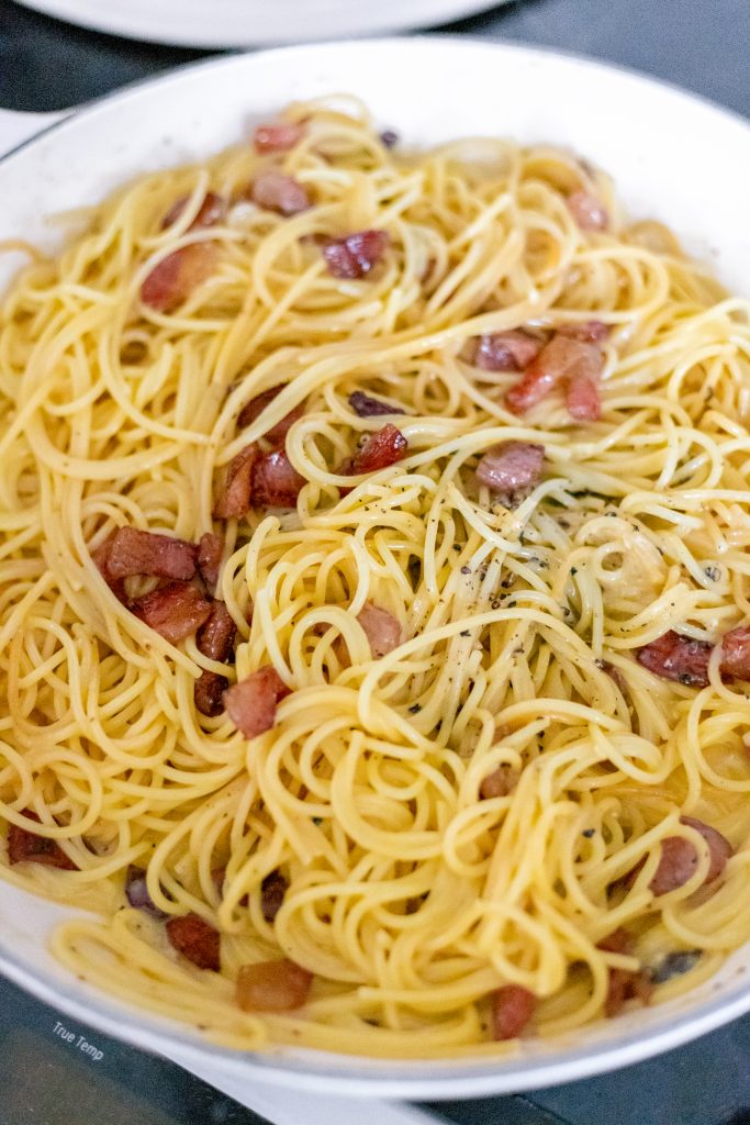 How to make carbonara: spaghetti in a yellow sauce with cubed guanciale (looks like bacon) in a white pan