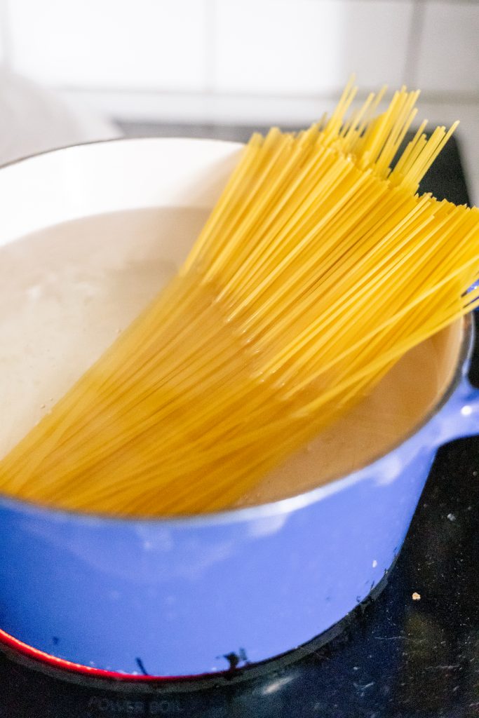 How to make spaghetti carbonara: spaghetti cooking in a blue pot on a stove.