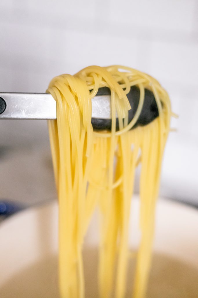 How to make spaghetti carbonara: tongs holding cooked spaghetti over a pot