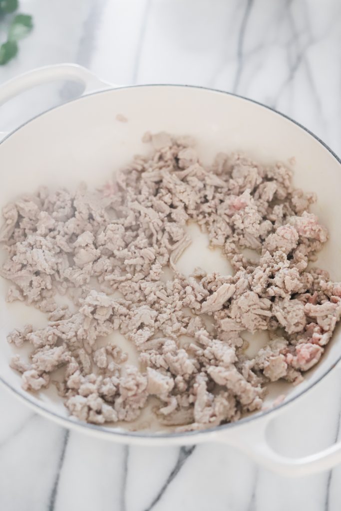Browned ground turkey in a white pan on a marble backdrop