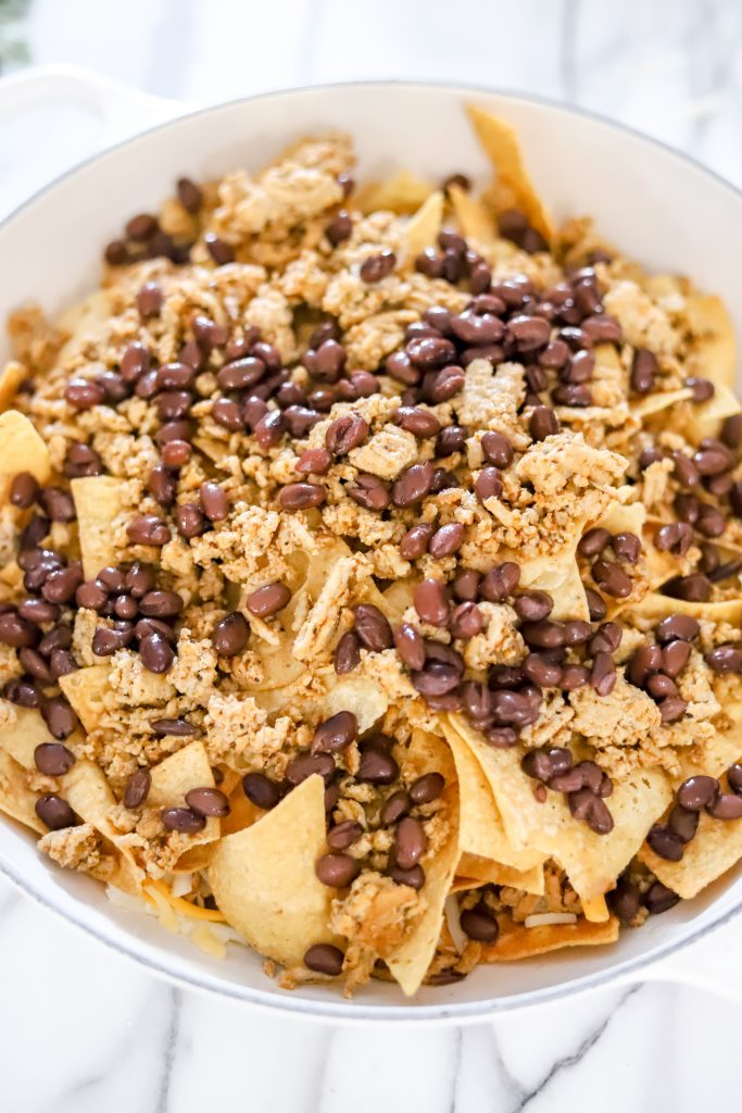 Tortilla chips on a white pan ontop of a marble backdrop with black beans and ground turkey ontop