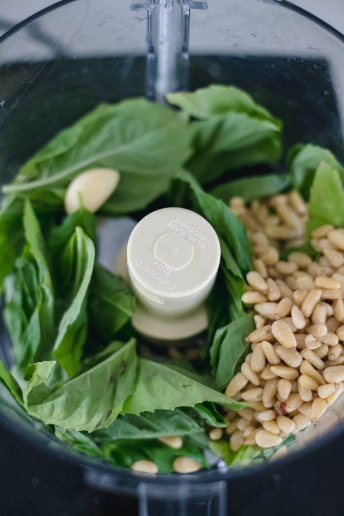 How to make basil pesto: pine nuts, basil leaves, and garlic cloves in a food processor.