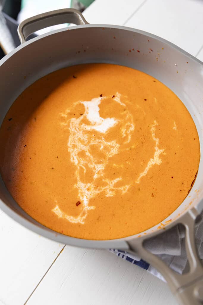 Creamy, orange sauce in a pan with a streak of heavy cream through it.