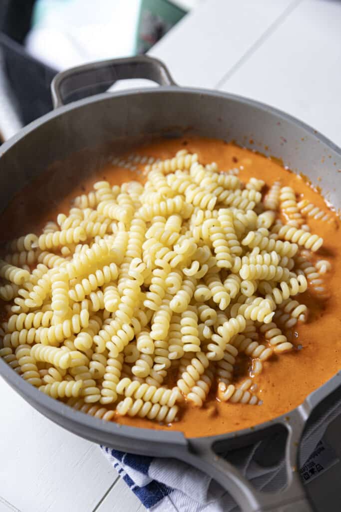 Hot pasta dumped into a pan with lots of orange sauce underneath it