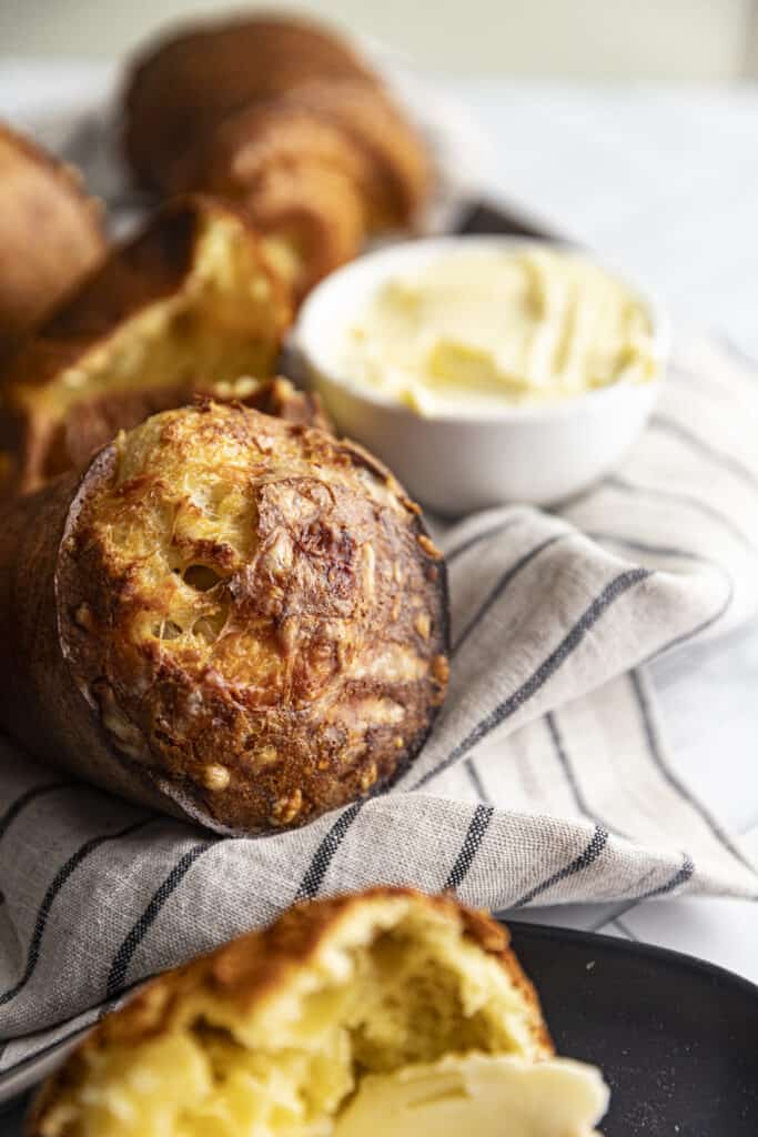 Zoomed in shot of popover on a gray linen towel with blue stripes with a butter knife and a small bowl of butter.