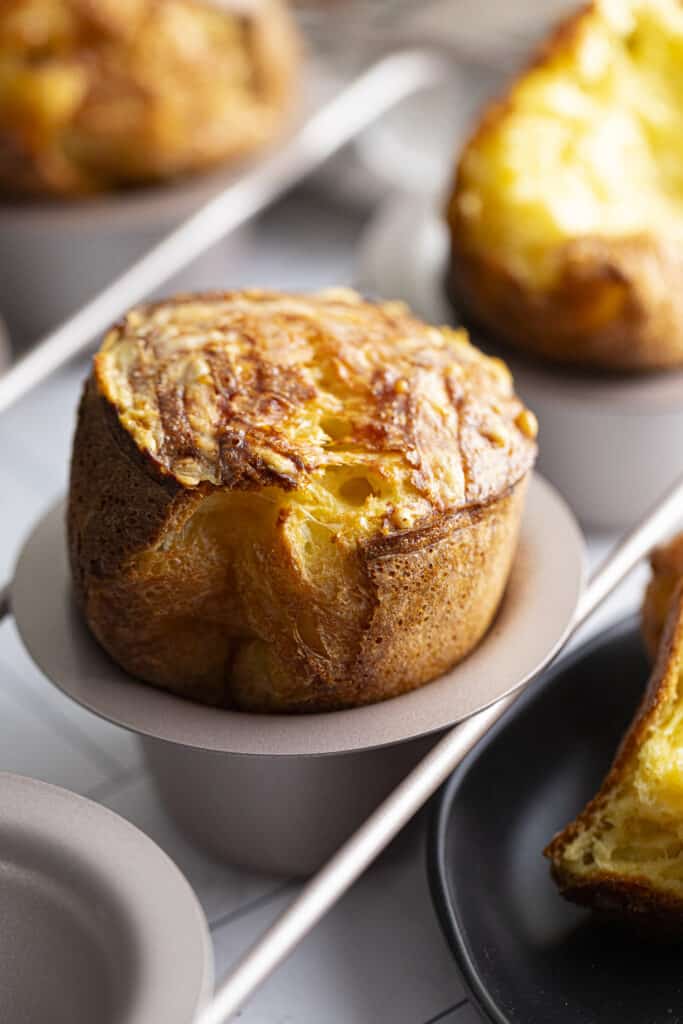 Zoomed in 45 degree photo of gruyere popover in a popover pan with others blurred in the background.