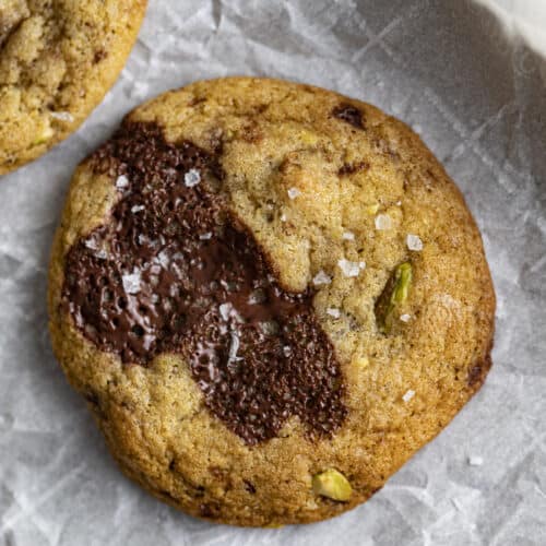 Overhead shot of chocolate chunk pistachio cookie on parchment paper on rimmed baking sheet.