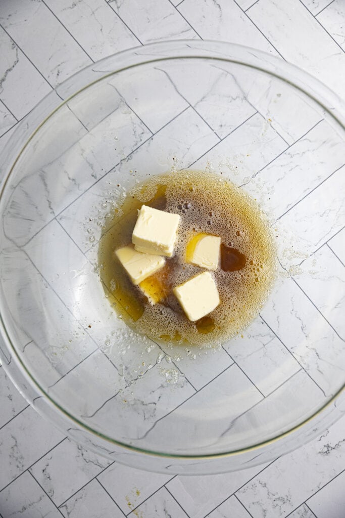 Overhead shot of melted brown butter in a glass bowl with unmelted pads of butter ontop.