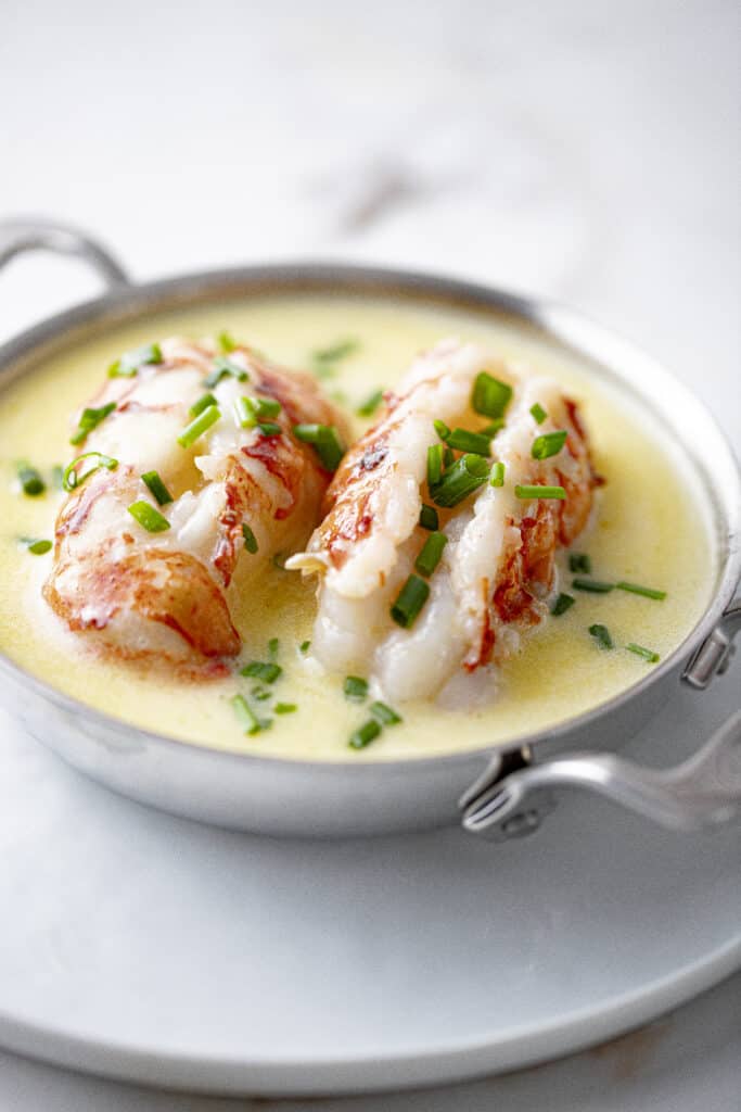 Butter poached lobster: lobster tails poached in butter in silver dish sprinkled with chopped chives.