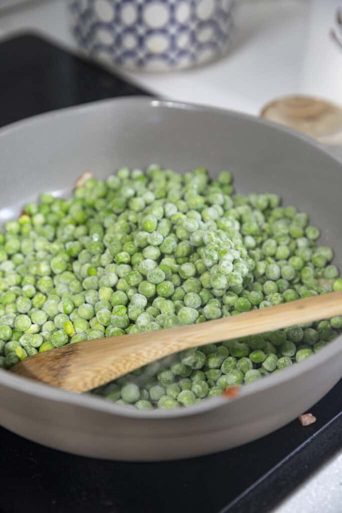 Overhead shot of frozen peas in a gray pan on the stove.