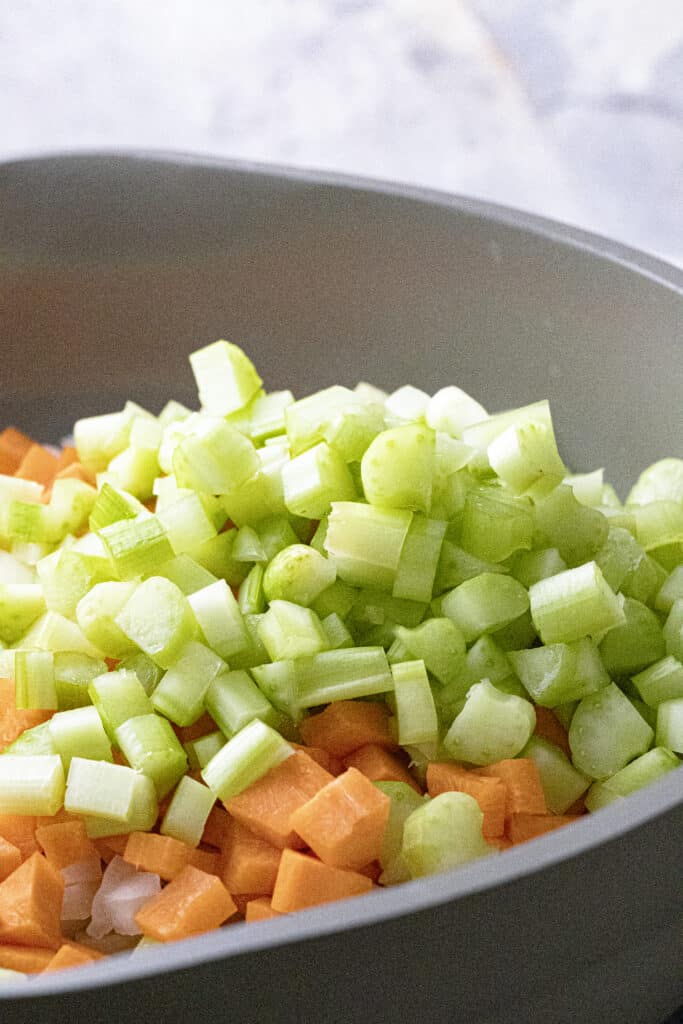 Raw, diced celery, ontop of raw, diced carrots ontop of raw, diced white onion in a pan.