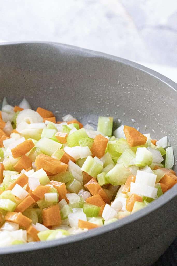 Diced celery, carrot, and white onion mixed in a pan with melted butter mid-cooking.