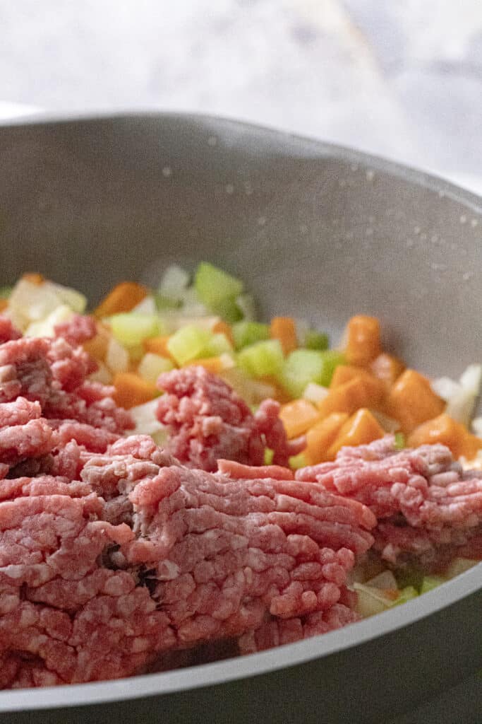Raw ground beef added to pan with diced carrots, celery, and onion.