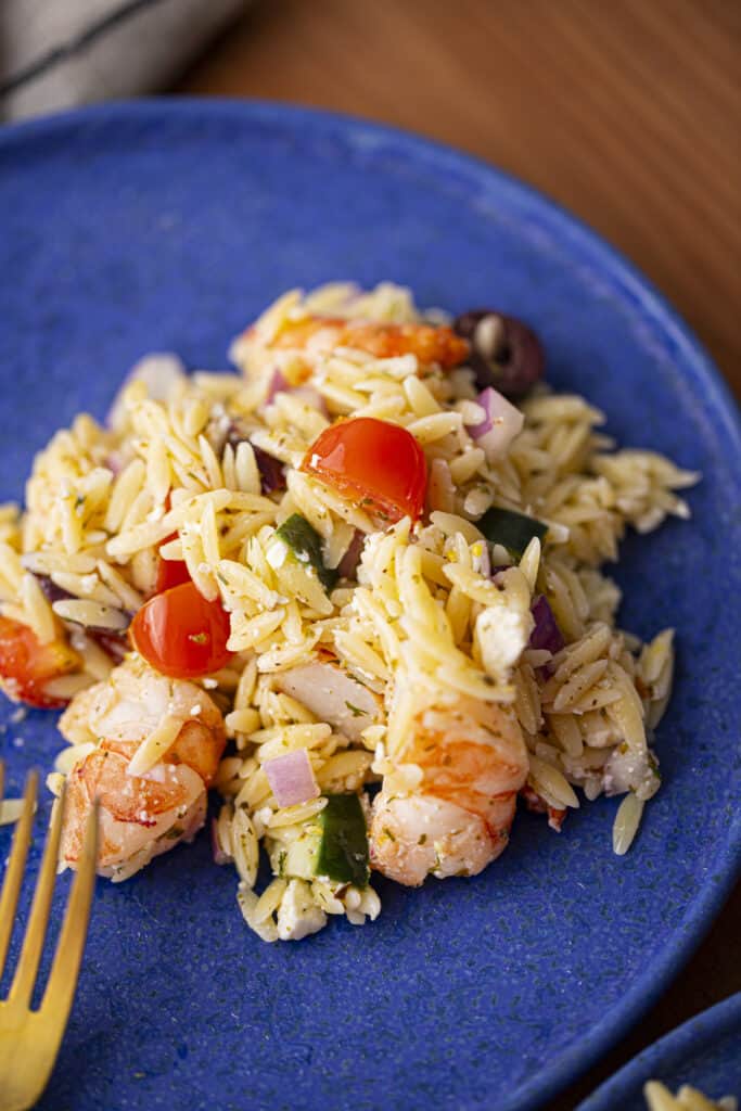 Mediterranean shrimp orzo salad on a blue plate with a gold fork.