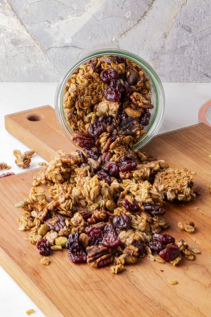 Zoomed out head on shot of a glass weck jar dumped out with pistachio granola falling out onto a wooden cutting board.