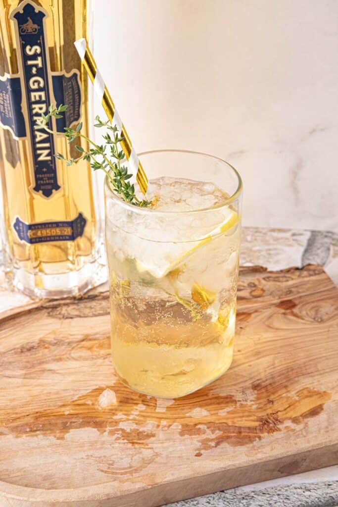 St-Germain Spritz with a gold straw on a wooden board. 