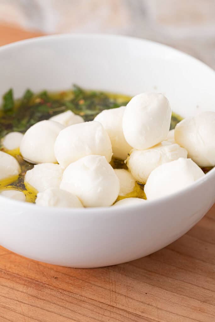 Adding mozzarella to herbed olive oil to make my marinated mozzarella balls recipe.