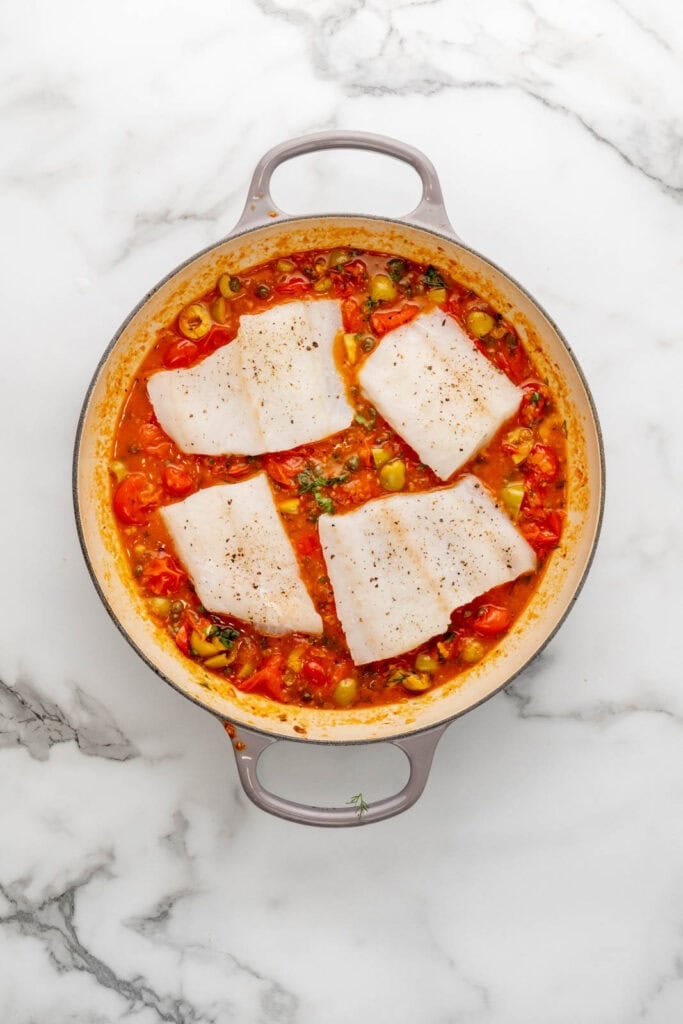 Baked fish fillets in a tomato and vegetable sauce, seasoned with herbs and spices.