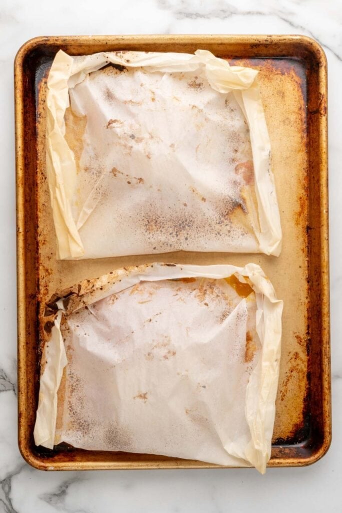 Closed parchment pockets on a baking sheet.
