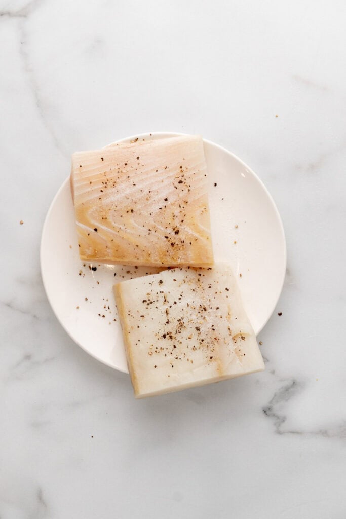 Halibut fillets with salt and pepper on a plate.