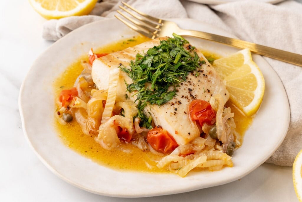Halibut on a plate with veggies and herbs.