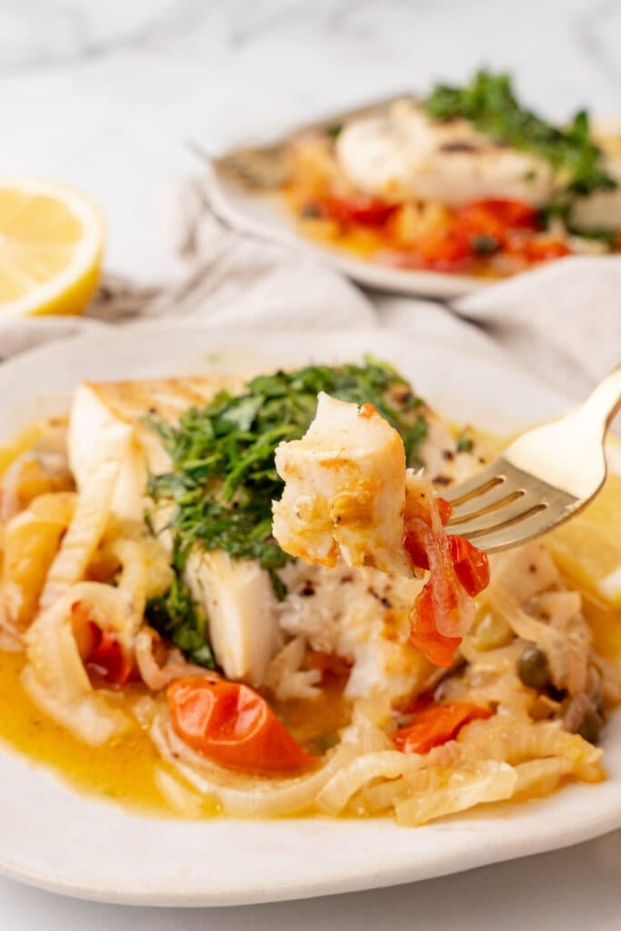 Halibut on a plate with veggies and herbs, with a fork.