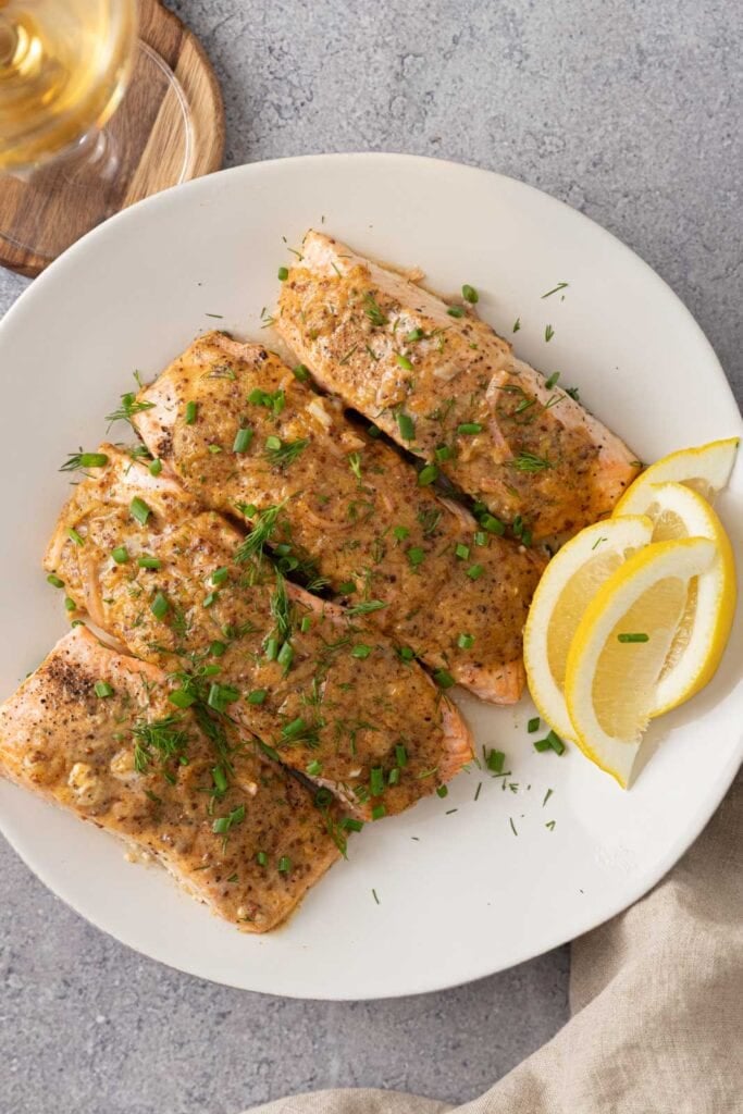 Dijon salmon on a plate with lemon, chives, and dill.