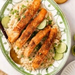 Coconut rice and salmon on a serving platter with limes and scallion.