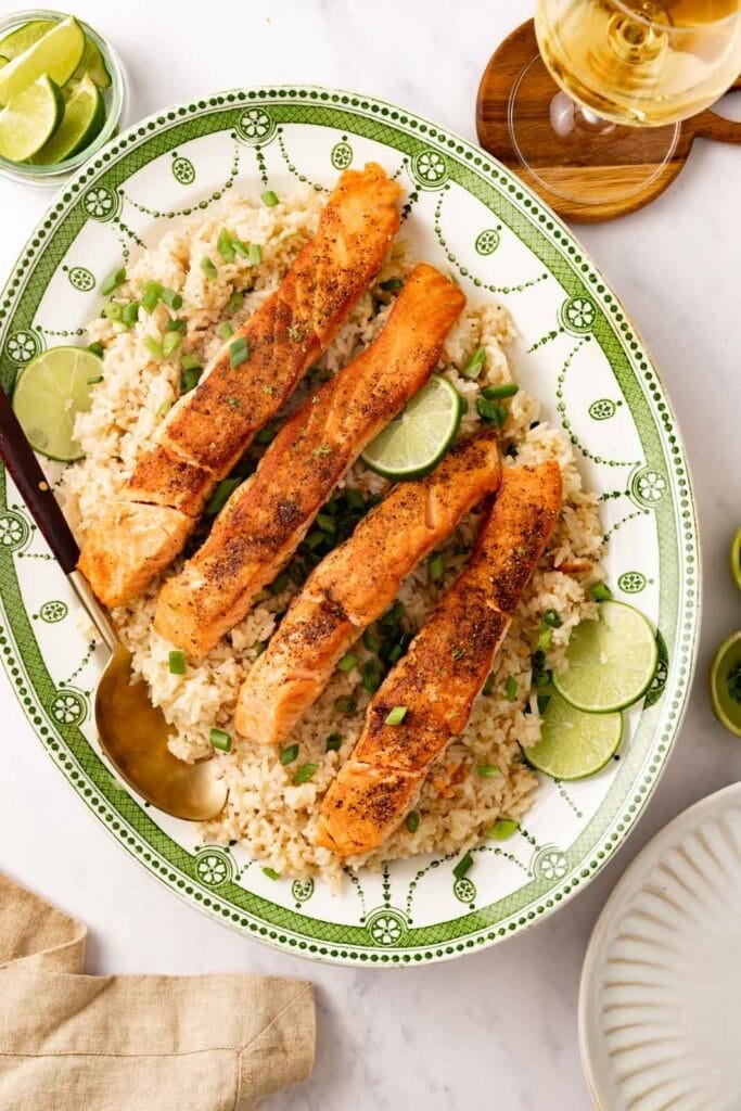 A serving platter with coconut rice and salmon with sliced scallions and limes.