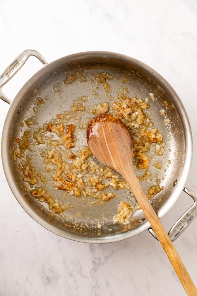 Sauteing minced shallot, garlic, and ginger in a stainless steel pan.
