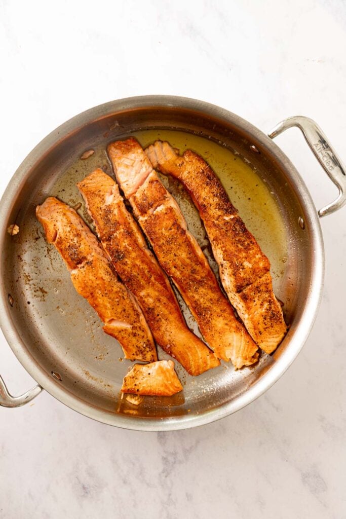 Seared salmon in a stainless steel pan.