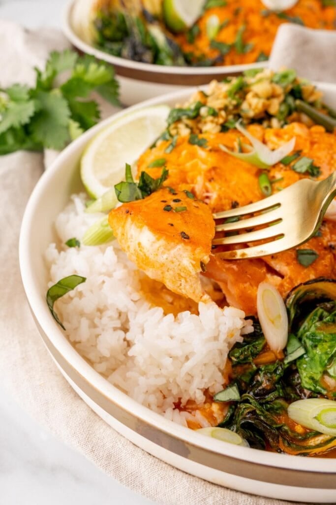 Salmon with coconut curry and rice in a bowl with lime and herbs.