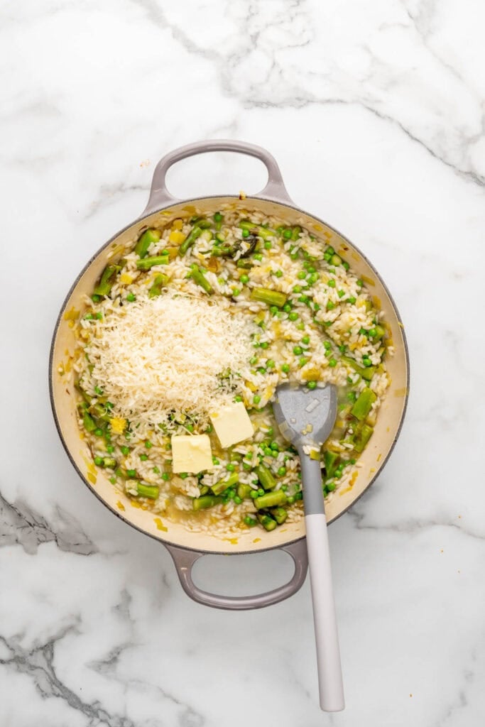 Spring risotto with asparagus and peas in a pan, adding butter and cheese.