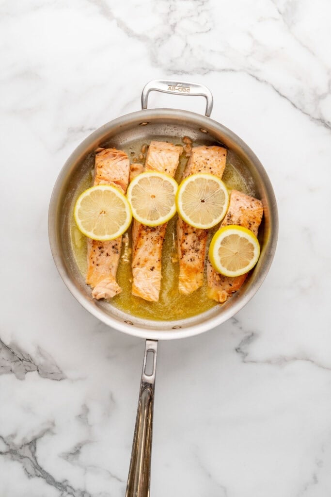 Searing salmon in a pan with lemon.