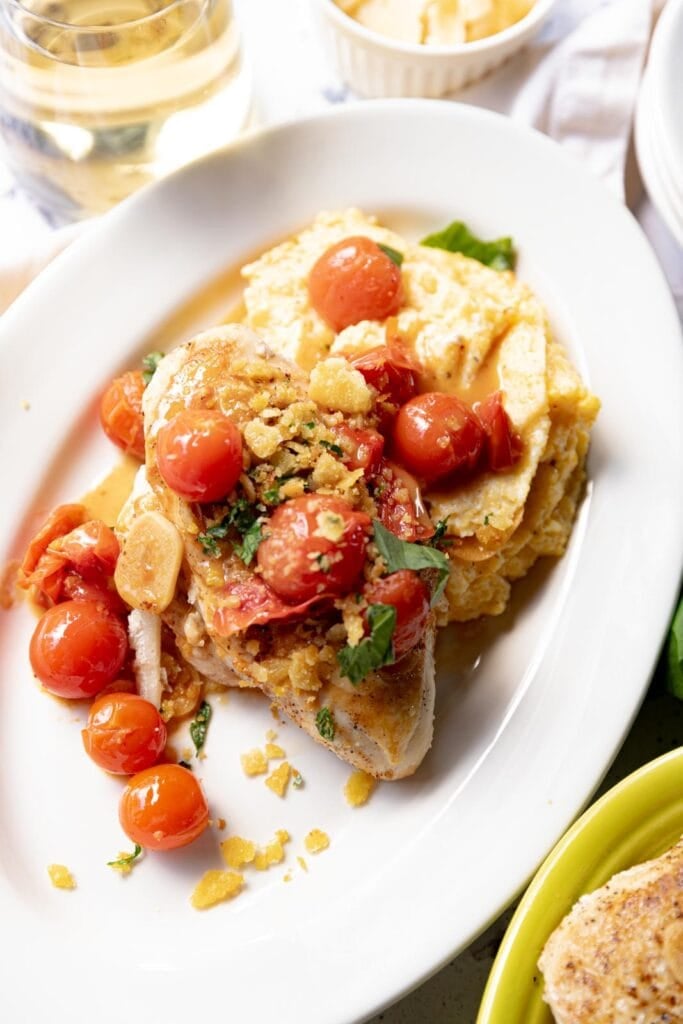 Seared chicken breasts with cherry tomato sauce and polenta on a plate.
