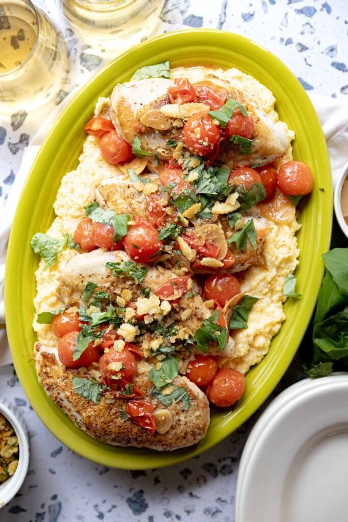 Seared chicken breasts with cherry tomato sauce and polenta on a serving platter.